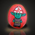 Toadstool Tom, a hand painted green woodland character rock with a red spotted toadstool hat, on a black and gold background
