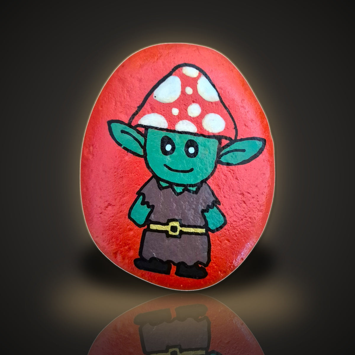 Toadstool Tom, a hand painted green woodland character rock with a red spotted toadstool hat, on a black and gold background