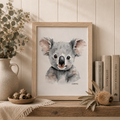 Framed artwork of a koala on a wooden shelf with decorative items.